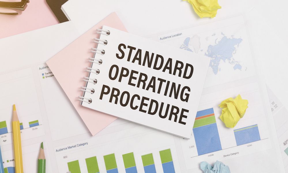 Standard Operating Procedure text on paper in open diary with spectacles, colourful push pin, pen and calculator on the wooden table - business and finance concept